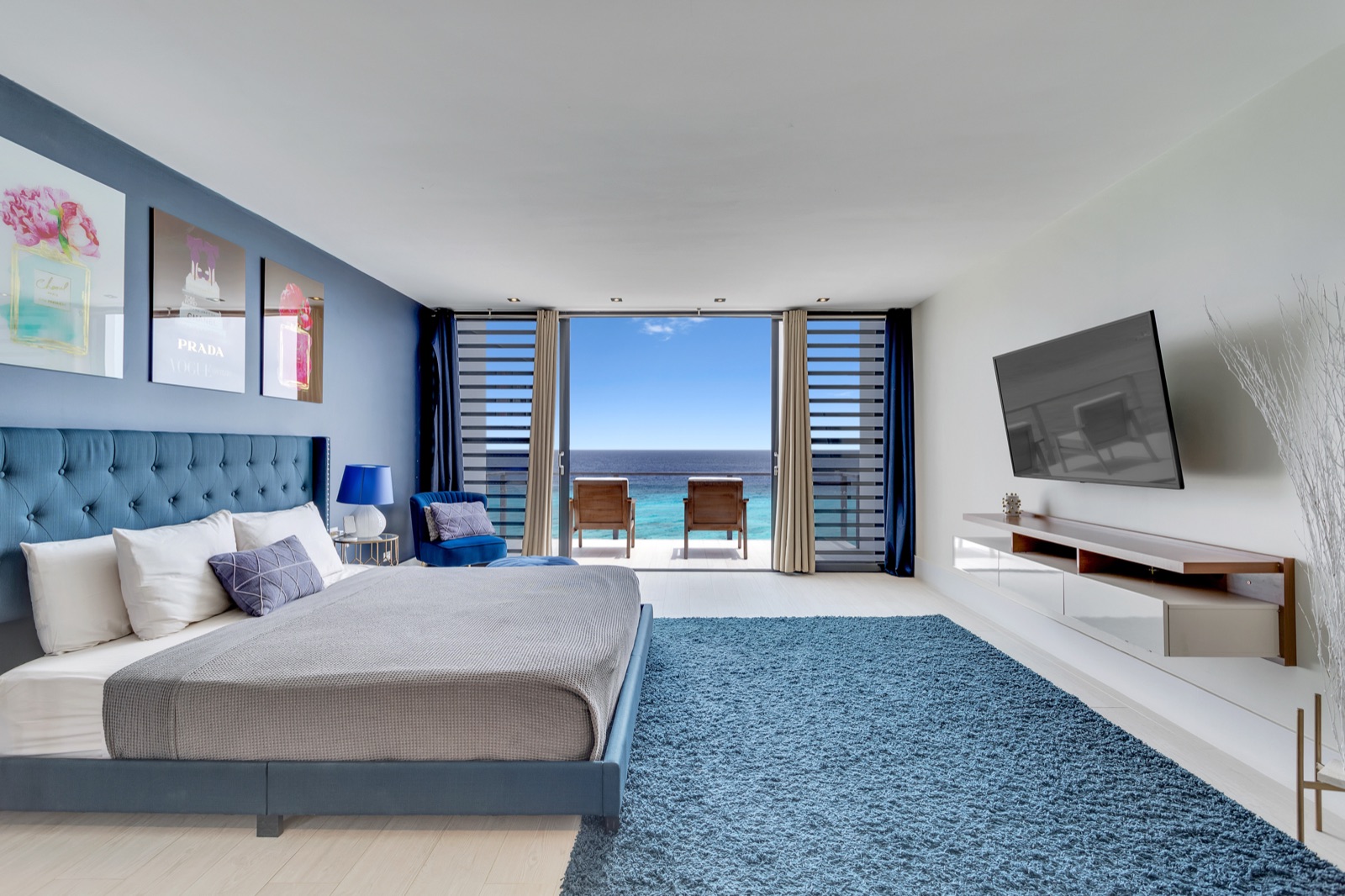 Luxury Bonaire villa master suite with a blue tufted king bed, modern floating console, and a private balcony with panoramic ocean views.